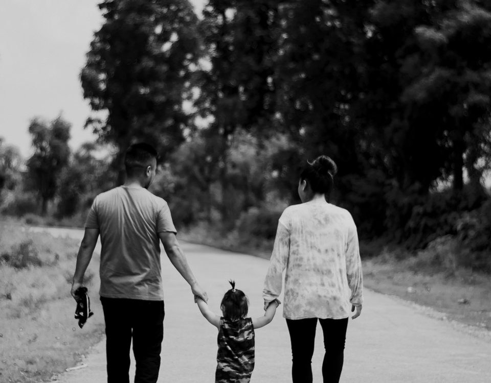 A man and woman walk holding a toddler's hands.