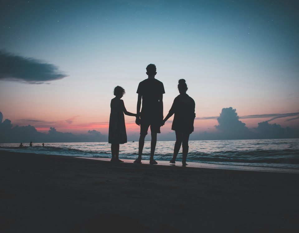 A family holds hands on the beach at sunset.