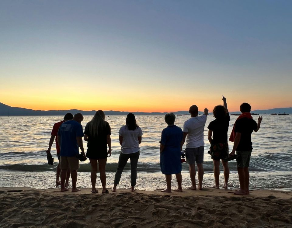 People standing on a beach at sunset.