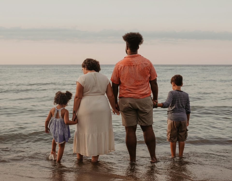 A family holds hands on the beach and looks out at the water.