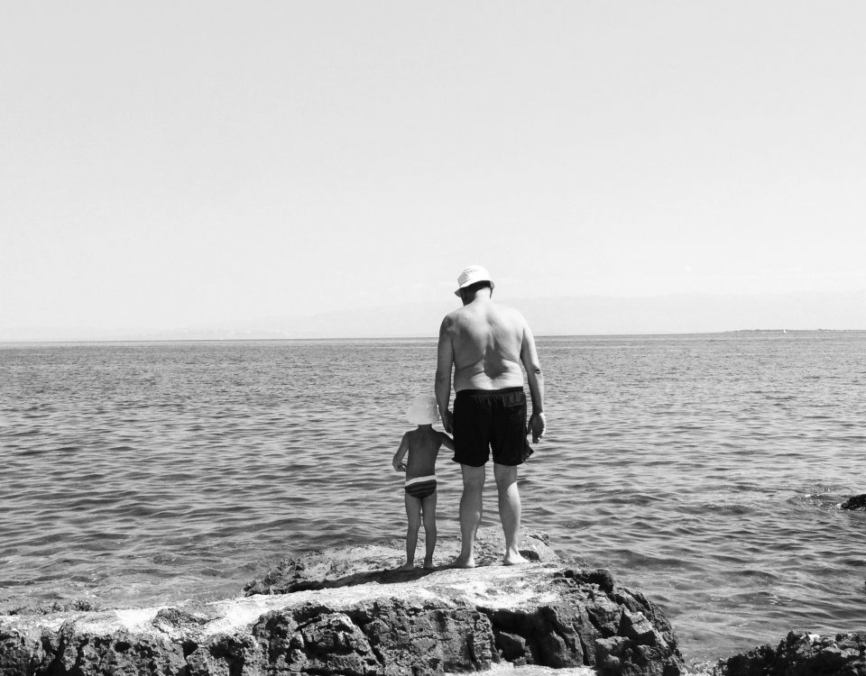 A man holds a boy's hand at the beach.