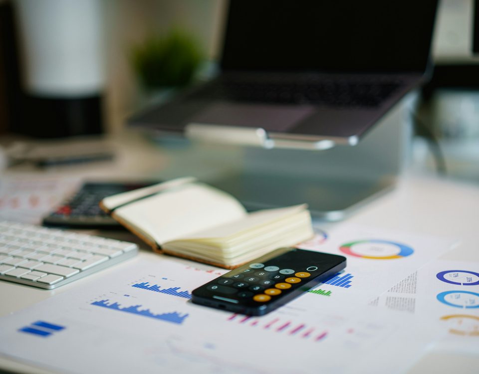 A calculator and laptop sit on papers.