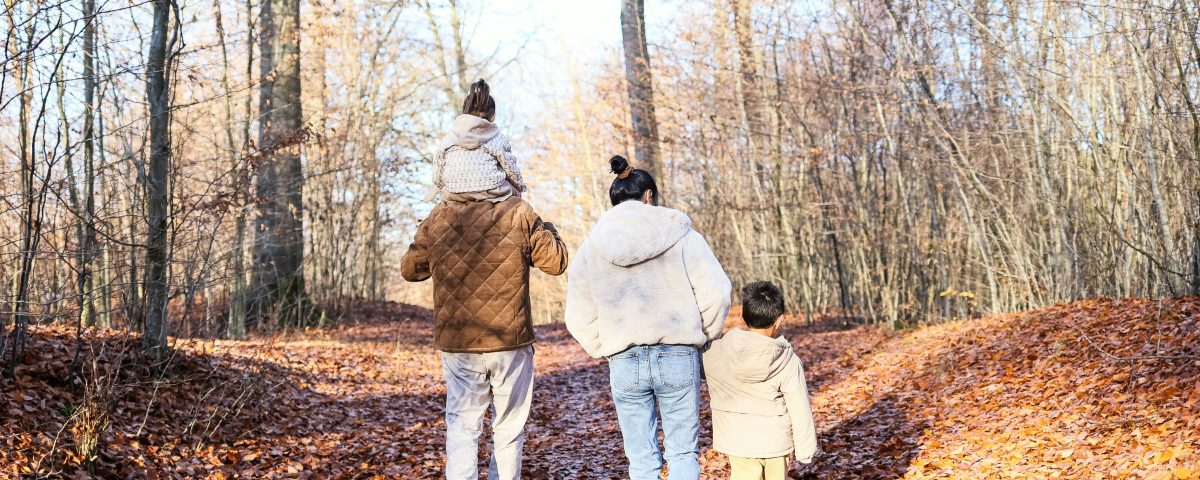 A family of four walks in the woods amidst bare trees.
