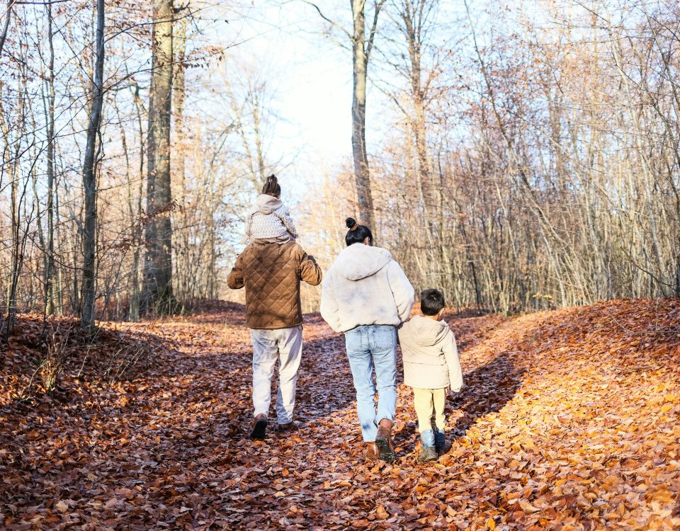 A family of four walks in the woods amidst bare trees.