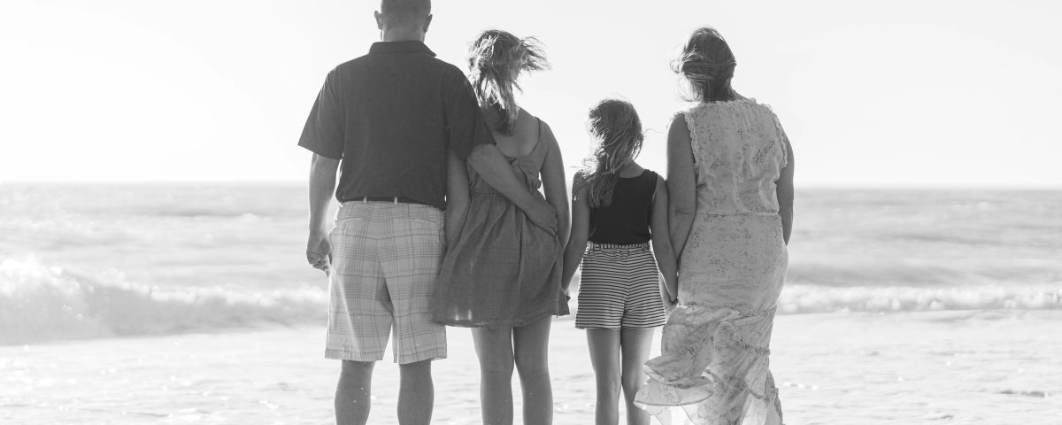 A black and white image of a family from behind on the beach.