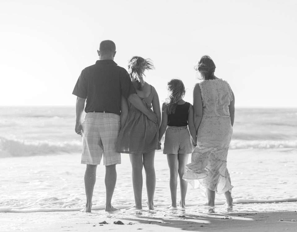 A black and white image of a family from behind on the beach.