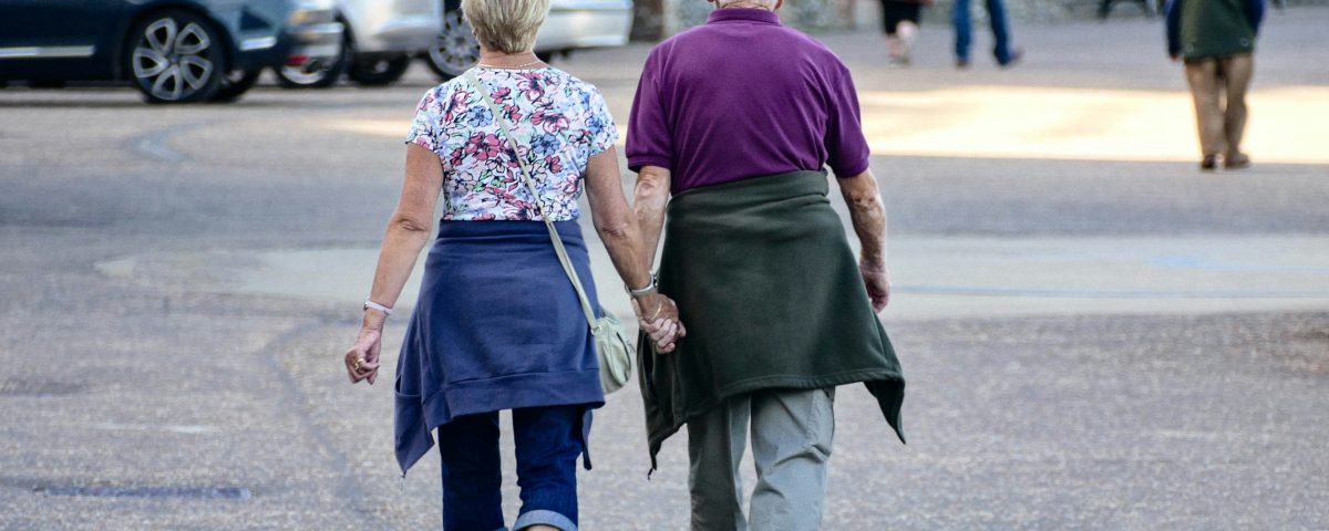 An older couple walks hand in hand down a street.