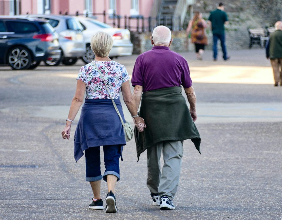 An older couple walks hand in hand down a street.