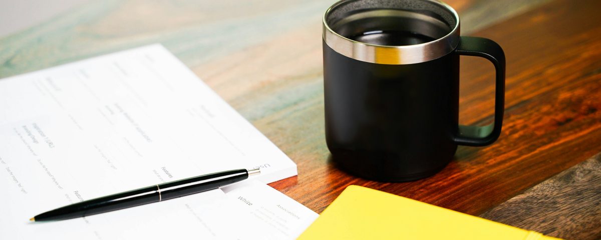Papers and a folder sit by a cup of coffee.