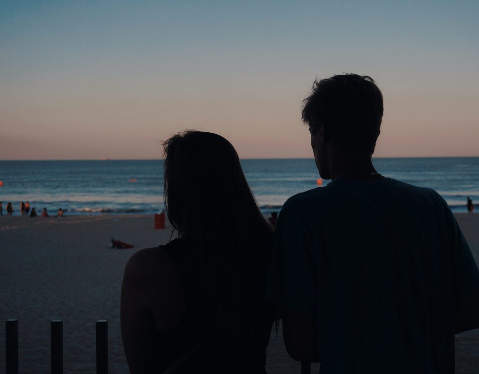 A man and woman watch the sunset on the beach.