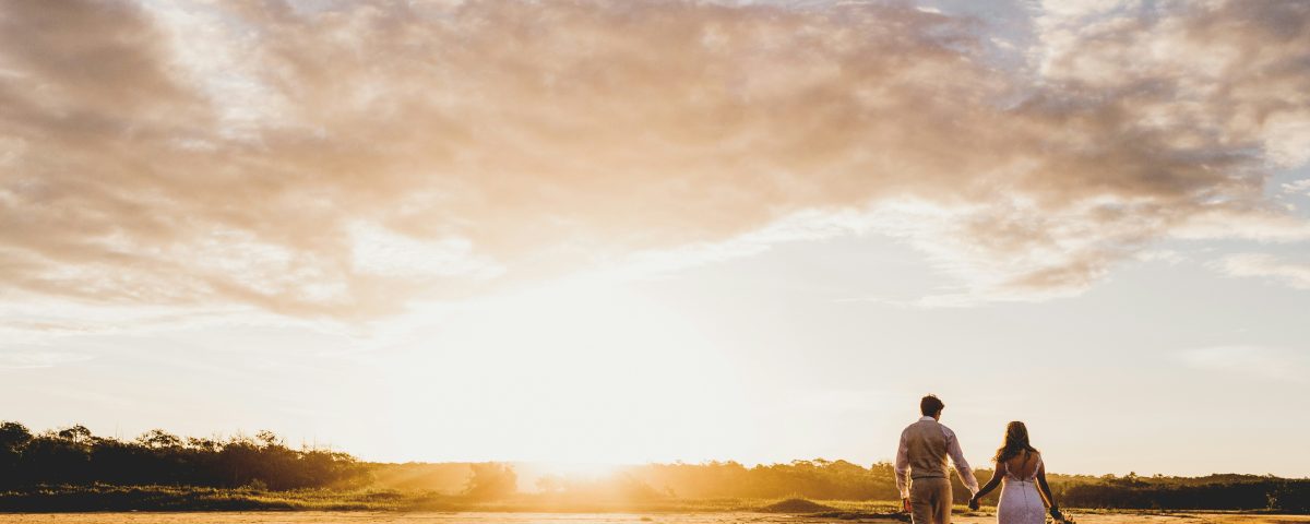 A bride and groom walk in a field.