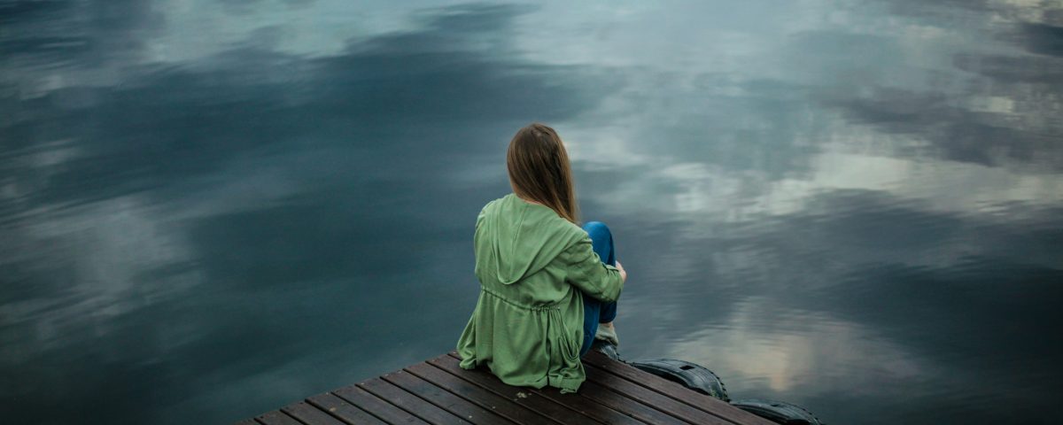A woman sits on a dock looking at the water.