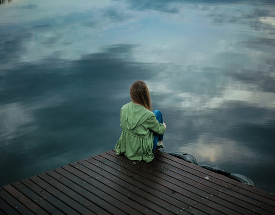 A woman sits on a dock looking at the water.