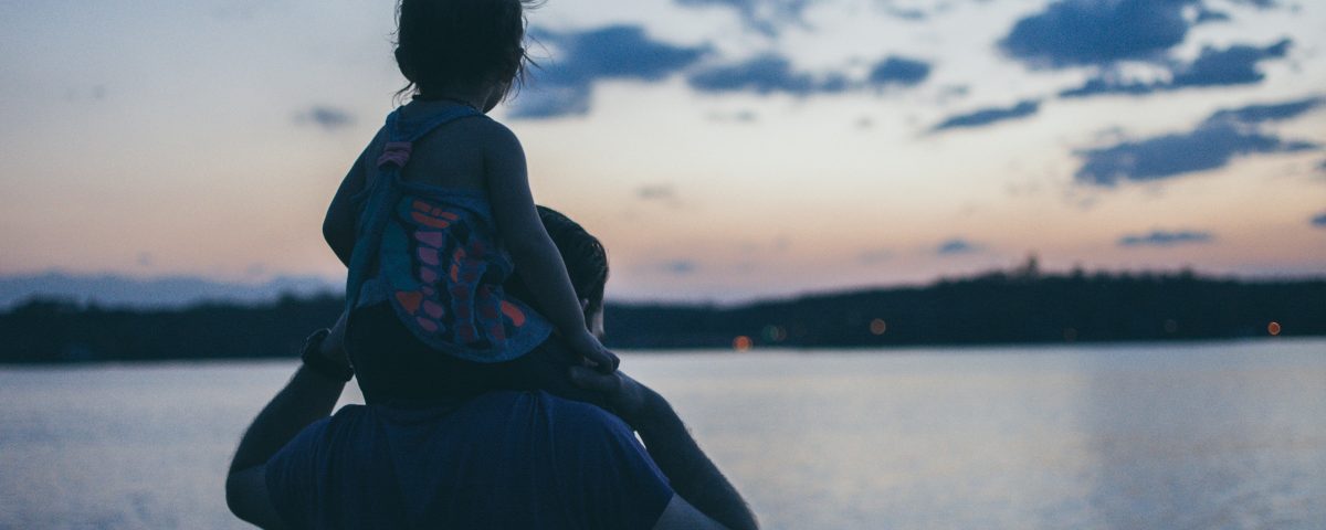A man holds a little girl on his shoulders.