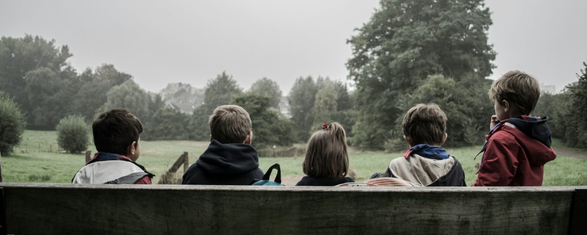 A view of kids sitting on a bench from behind.