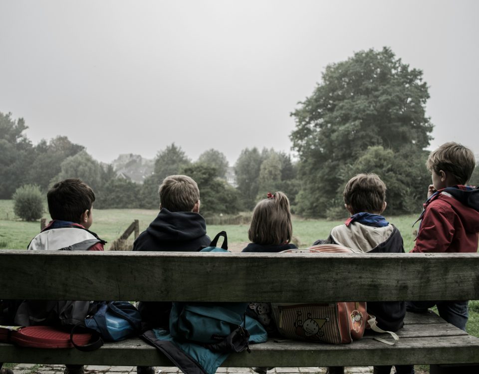 A view of kids sitting on a bench from behind.