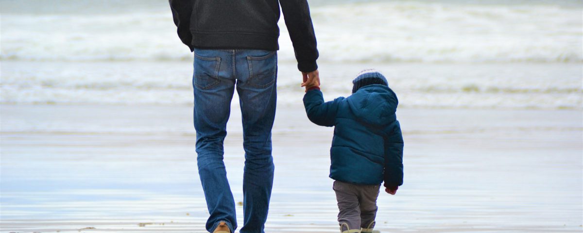 A father and child walk on a beach.