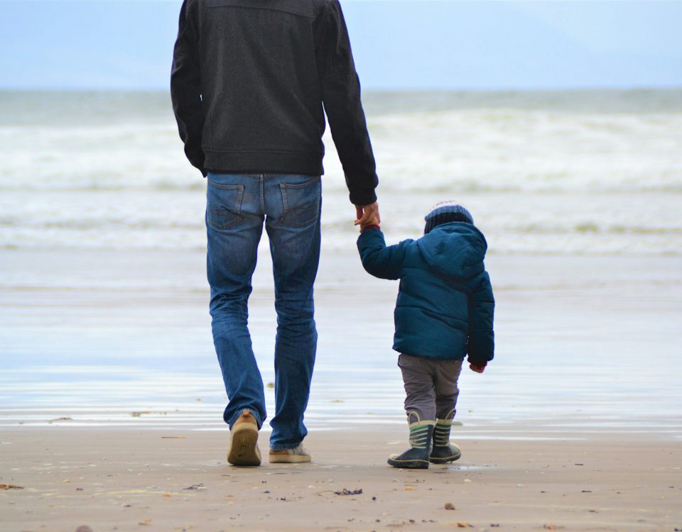 A father and child walk on a beach.