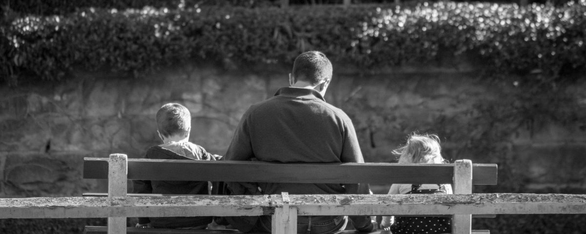 A man sits on a bench with two young kids.