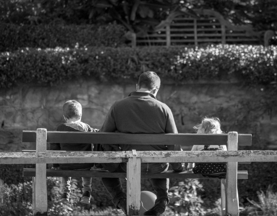 A man sits on a bench with two young kids.