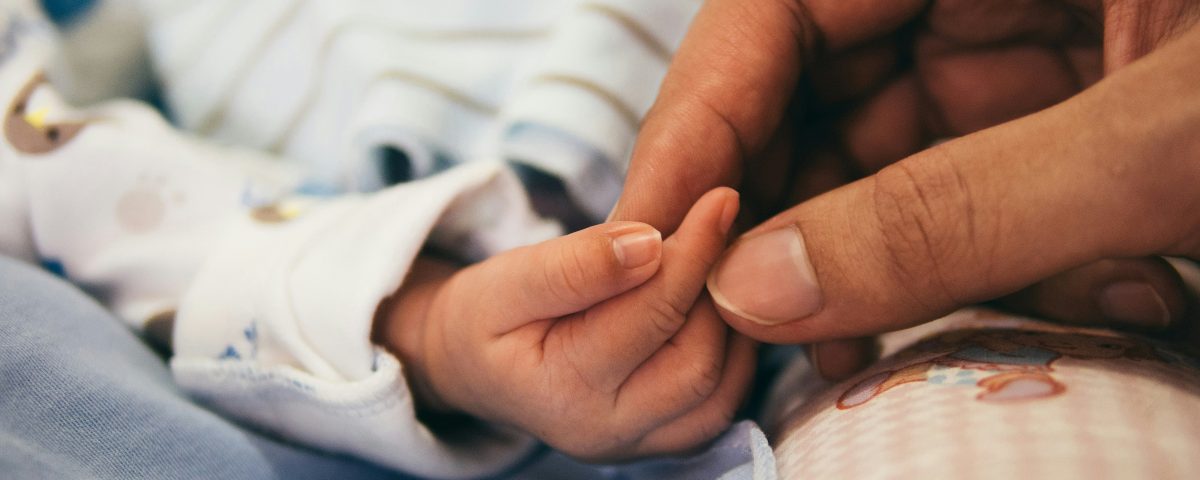 A mom's hand holds a baby's hand.