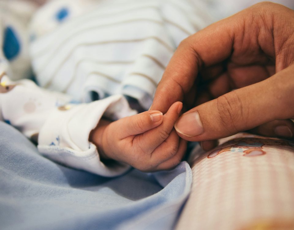 A mom's hand holds a baby's hand.