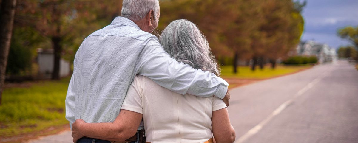 An older couple walks down a road from behind.