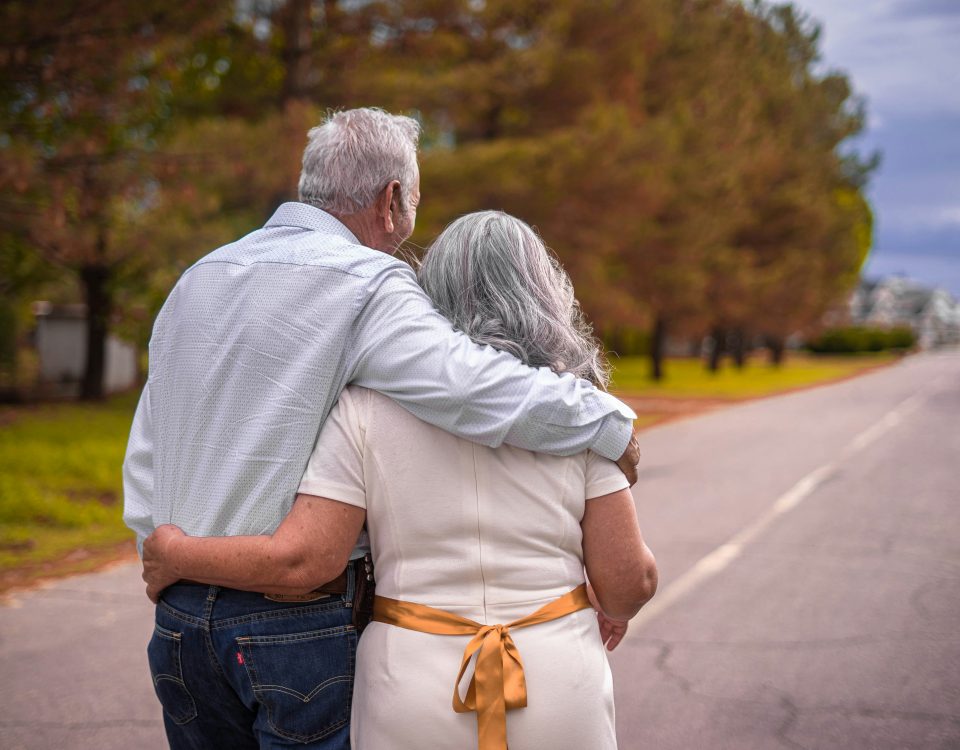 An older couple walks down a road from behind.